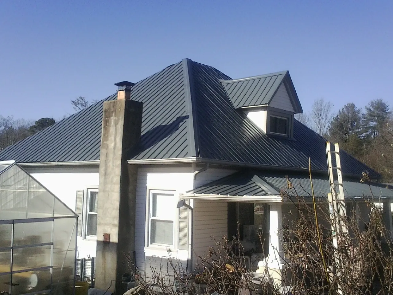 Dark blue standing seam metal roof on a white farmhouse with dormer — Slate & Tile Roof Repair by Roofing Brothers in North Miami Beach