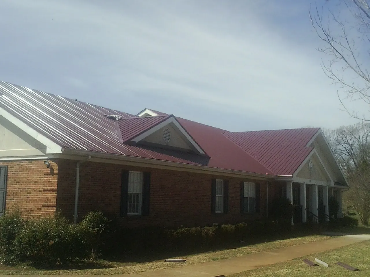 Red metal roof with gabled entries on a long brick building, from a Hail Damage Roof Repair job in North Miami Beach