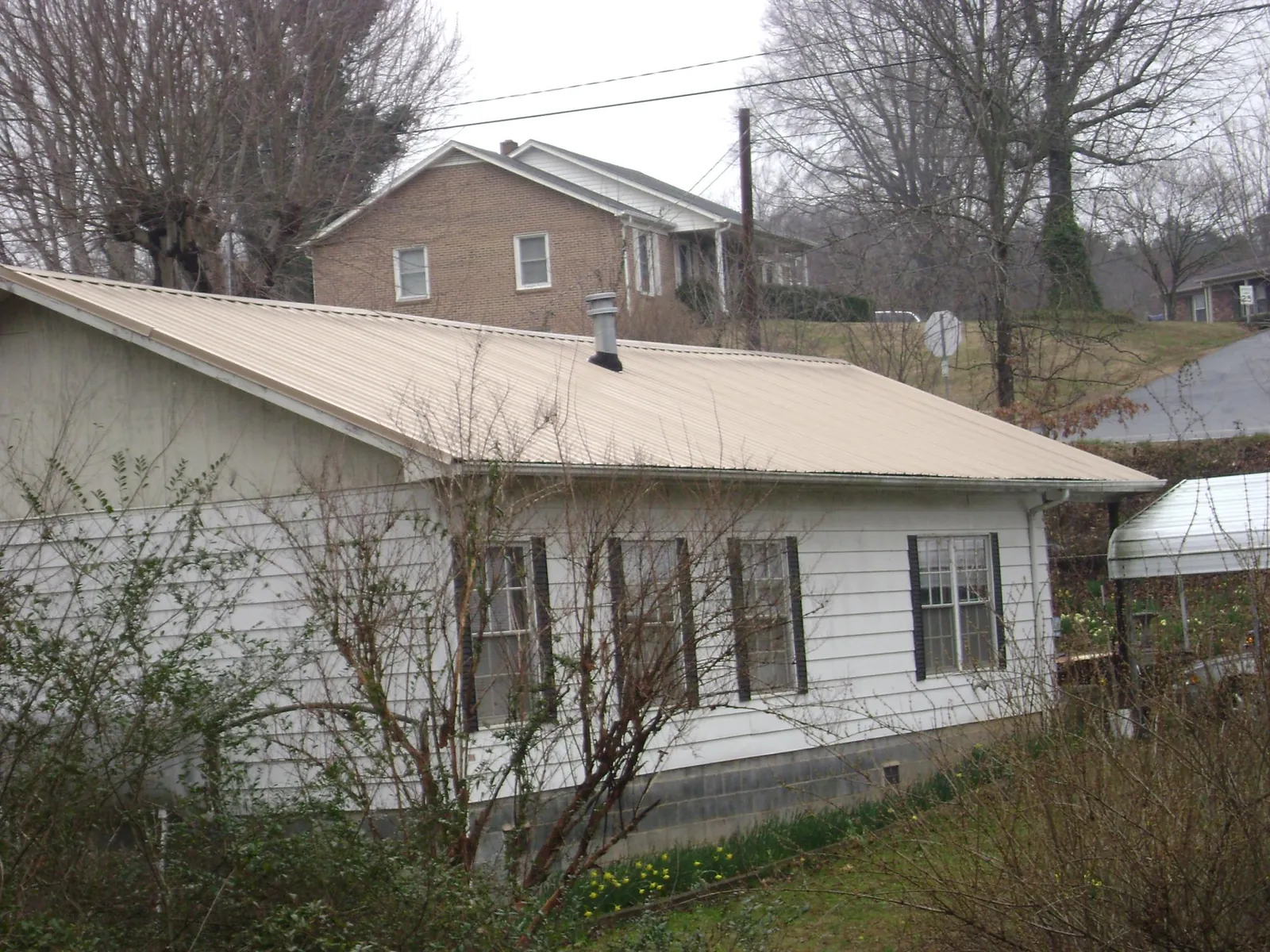 Tan metal roof on a white sided house set into a hillside — Commercial Roofing by Roofing Brothers in North Miami Beach
